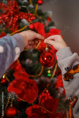 Children decorate a Christmas tree with red ornaments and festive decorations during the holiday season