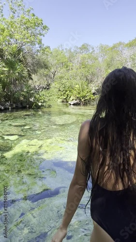 Heart Cenote in Mexico with crystal-clear waters and visible stones. A person happily jumping into the water. Warm, blue-green waters perfect for a family vacation in Yucatán, Mexico.