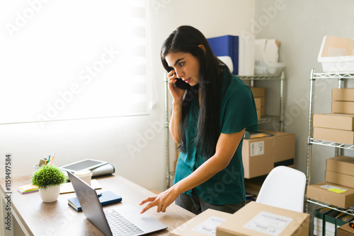 Latin businesswoman multitasking in warehouse with cardboard boxes, managing her ecommerce business