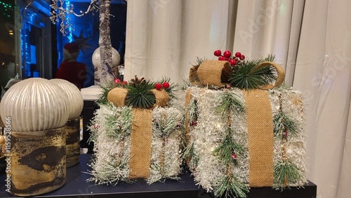 A pair of beautifully wrapped holiday gifts is arranged on a table. The gifts feature natural elements like greenery and berries, evoking a festive atmosphere. photo