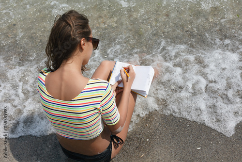 female makes notes and sitting on the beach photo