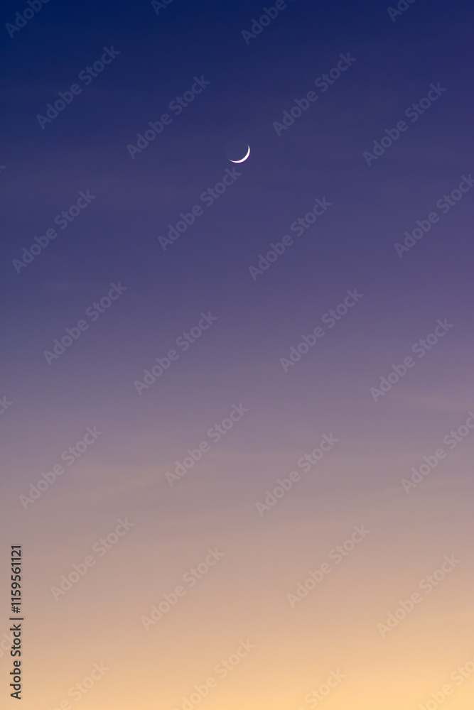 Purple to yellow gradient sky with thin crescent moon during sunset time