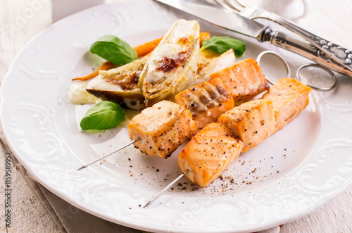 Traditional grilled salmon skewer with chicory salad, carrots and bechamel sauce served as close-up on a classic design plate photo