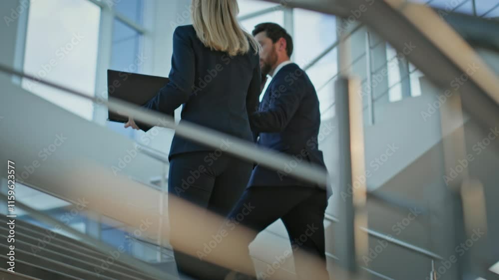 Two colleagues walking upstairs corporate office building. Elegant businesswoman