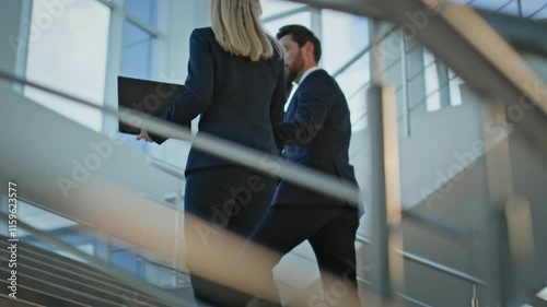 Two colleagues walking upstairs corporate office building. Elegant businesswoman
