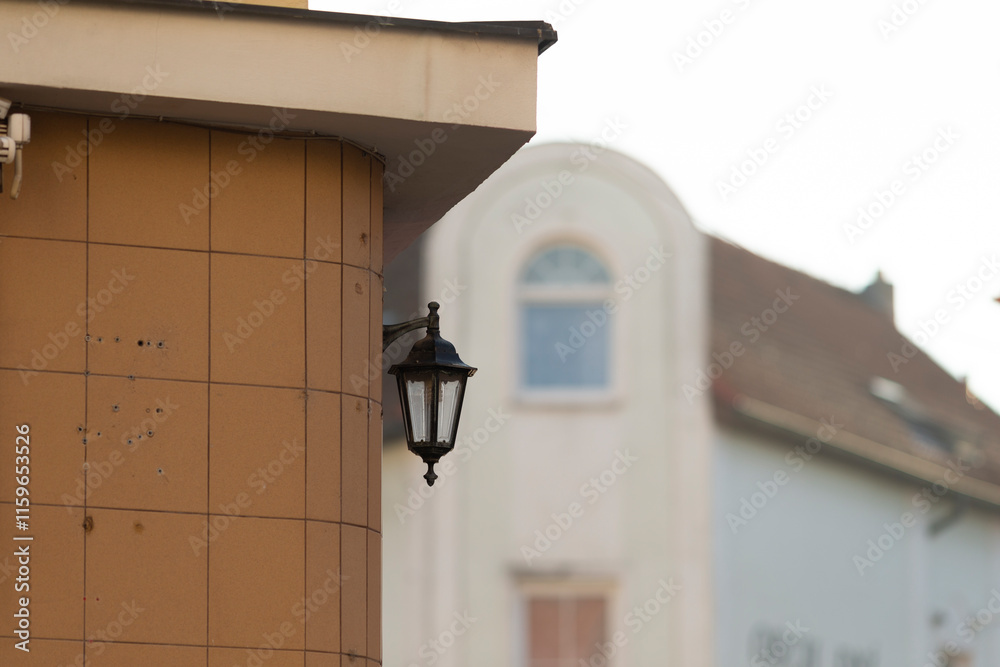 A picturesque corner of a building featuring an elegant hanging lantern, with a residential structure visible in the background A picturesque corner of a building featuring an elegant hanging lantern, with a residential structure visible in the background