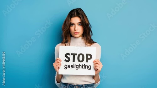 Young sad woman with Stop Gaslighting sign on blue background. Concept of mental health and manipulation in abusive relationships with a narcissist partner or co-worker. Slow motion zoom out.