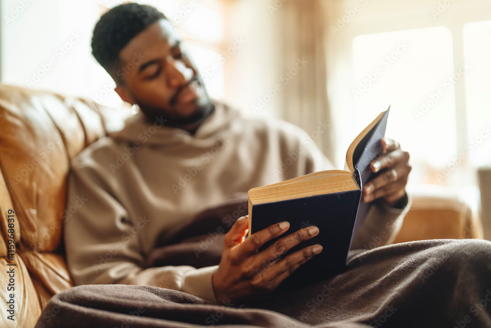 Man enjoys quiet reading time on a cozy couch in a sunlit living room during the afternoon