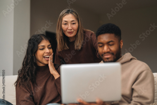 Three friends share laughter and excitement while watching content on a laptop in a cozy living room