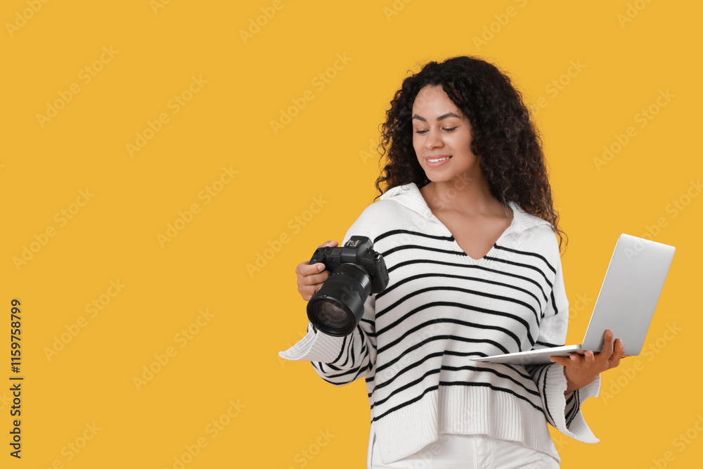 Fototapeta premium Female African-American photographer with camera and laptop on yellow background