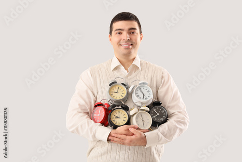 Young man with alarm clocks on light background. Time management concept photo