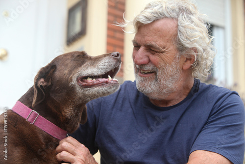 portrait of cheerful senior man sitting with dog outdoors by his house in the garden 