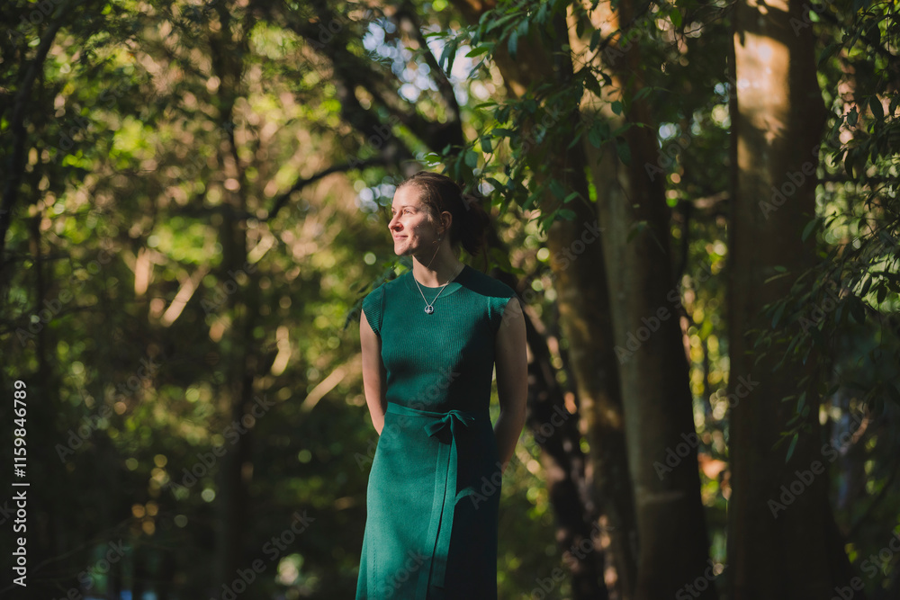 A woman in a green dress stands amidst tall trees in soft sunlight, her smile radiating warmth and her surroundings rich with forest tones and depth A woman in a green dress stands amidst tall trees in soft sunlight, her smile radiating warmth and her surroundings rich with forest tones and depth