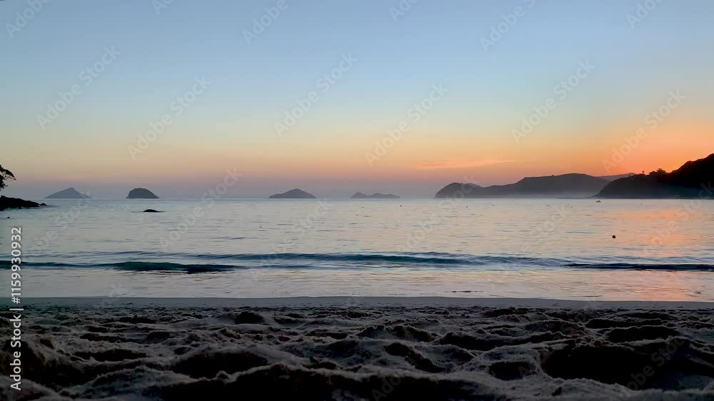 Fim de tarde após o pôr do sol, mar bastante tranquilo e o céu colorido. No fundo, , quatro ilhas conhecidas do litoral norte: Ilha Montão de Trigo, Ilha dos Gatos, Ilha das Couves e Ilha As Ilhas.