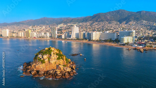 Aerial view of Acapulco Bay in front of the rocky island Farallon del Obispo. Some people swimming in the sea from the beach to the island in front of the hotel zone.