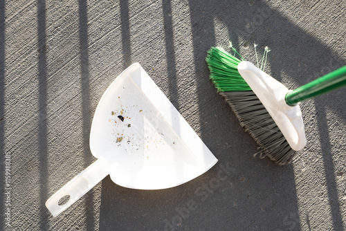 White plastic broom and dustpan on the floor with some collected garbage