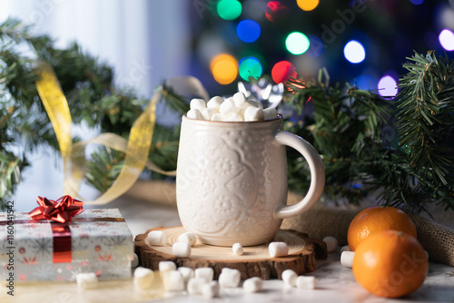 White cup of a hot chocolate with marshmallows on top, Christmas decorations and a Christmas tree as a background with bokeh. Warm Holidays season
