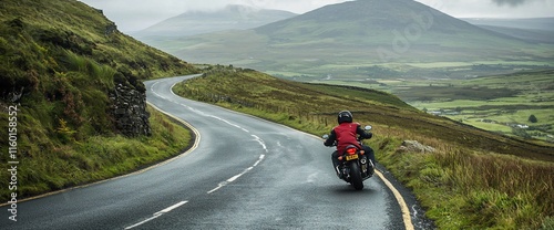 Motorcyclist rides scenic winding road through lush green hills and valleys.