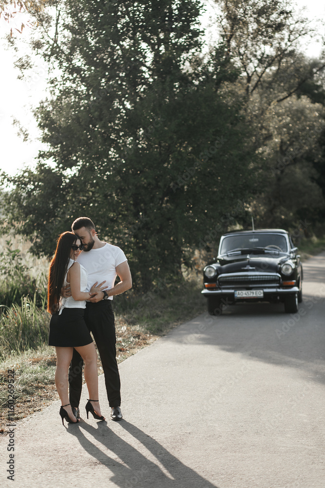 couple standing on the road. A man and a woman hug. The man is wearing a white T-shirt and black trousers, and the woman is wearing a white top and black skirt. couple standing on the road. A man and a woman hug. The man is wearing a white T-shirt and black trousers, and the woman is wearing a white top and black skirt.
