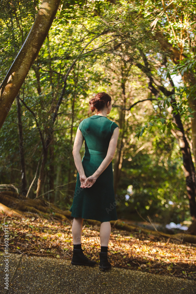 A young woman stands gracefully in a forest clearing, wearing a green dress and black boots. Sunlight filters through the dense trees, creating a serene, natural atmosphere of dappled light and shadow A young woman stands gracefully in a forest clearing, wearing a green dress and black boots. Sunlight filters through the dense trees, creating a serene, natural atmosphere of dappled light and shadow