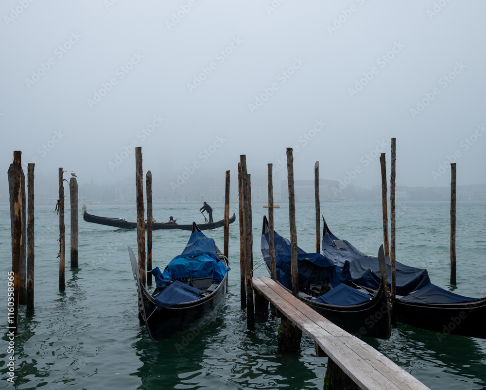 Gondolas tied to wooden columns on the waters of the Venetian canal. Gondolas tied to wooden columns on the waters of the Venetian canal.