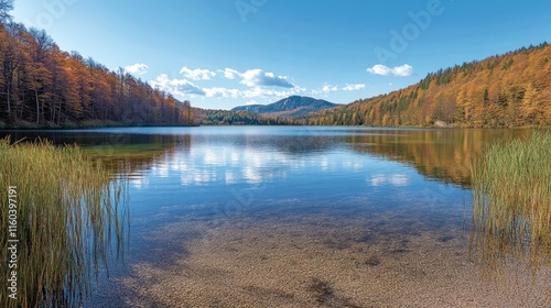 Serene autumn lake landscape with clear water reflecting colorful trees and a mountain range in the background.