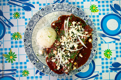 Traditional enchiladas with Oaxaca cheese, red mole and rice. Enchiladas are a dish from Mexican cuisine made with rolled or folded corn tortillas.