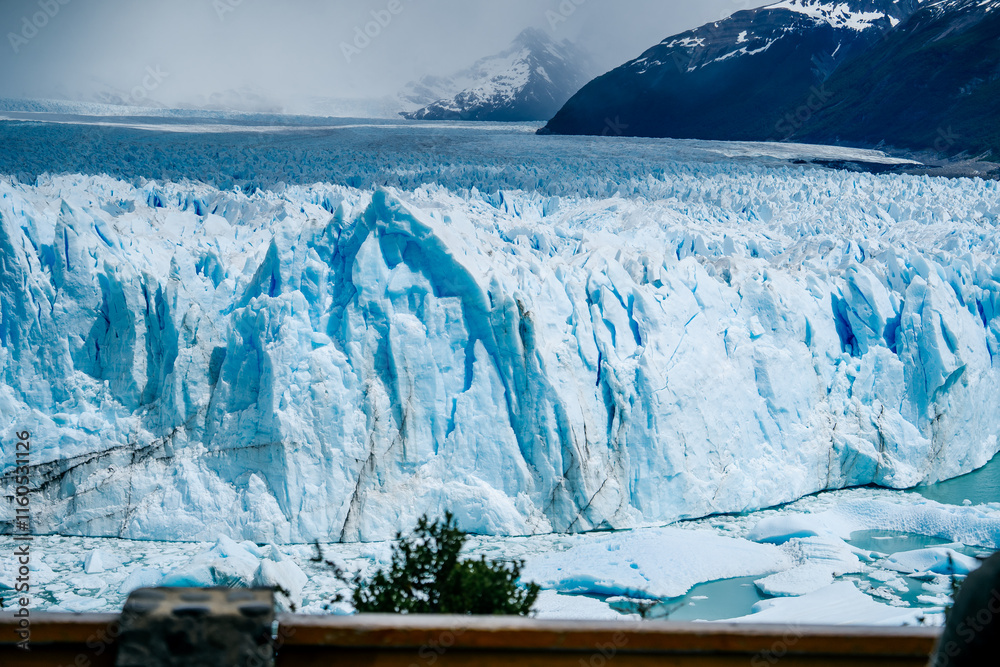 Φωτογραφία A breathtaking view of the Perito Moreno Glacier in Patagonia, Argentina, showcases its icy blue walls contrasting with lush green vegetation and vibrant red flowers in the foreground