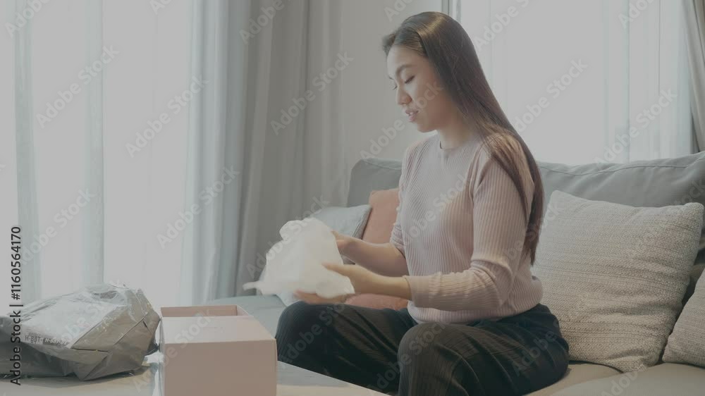 A young woman unwraps a package in her cozy living room, showcasing the excitement of receiving a delivery. The serene environment highlights the joy of unboxing and discovering new items. A young woman unwraps a package in her cozy living room, showcasing the excitement of receiving a delivery. The serene environment highlights the joy of unboxing and discovering new items.