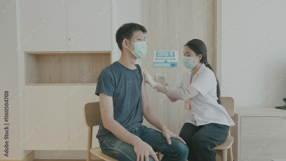 A man is getting a shot from a nurse. The nurse is wearing a mask and the man is wearing a blue shirt A man is getting a shot from a nurse. The nurse is wearing a mask and the man is wearing a blue shirt