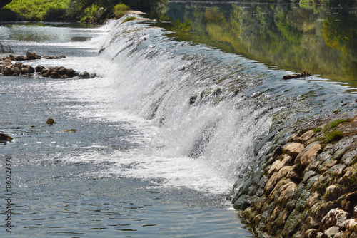 A picturesque view of the Dobra River near Jaskovo, featuring a small dam creating a gentle waterfall, lush greenery lining the banks photo