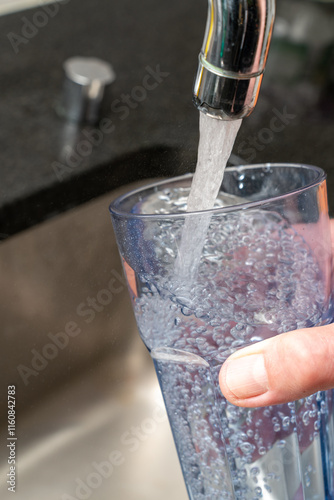 Filling a glass of fresh cool water at the tap of the kitchen sink. Concept of good water quality.. Close up, vertical photopraph.