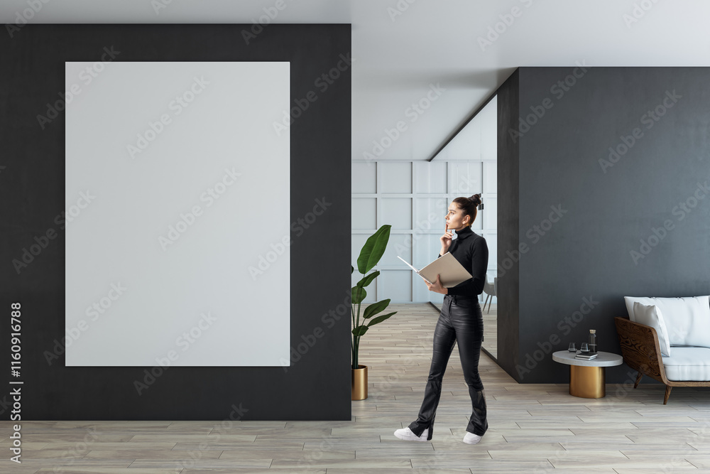 Obraz premium Modern office interior with a businesswoman holding a folder near a large blank poster on the dark wall, wooden floor, and clean design.