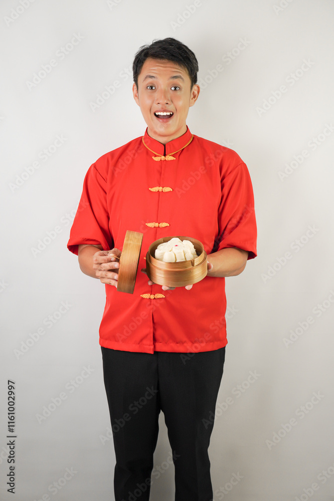 Handsome young asian man wearing red traditional chinese clothing is opening baozi dimsum steamer lid, isolated over white background. Concept for Lunar New Year Party. Handsome young asian man wearing red traditional chinese clothing is opening baozi dimsum steamer lid, isolated over white background. Concept for Lunar New Year Party.