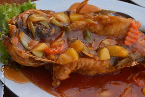 A classic sweet and sour fish dish features crispy fried fish topped with a vibrant sauce made from vinegar, sugar, and tomato. Garnished with bell peppers, onions, and pineapple for extra flavor. 