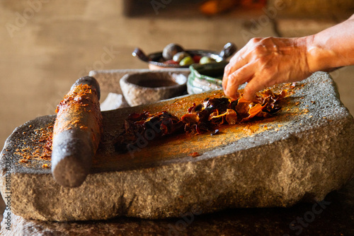 Woman from an indigenous community in Oaxaca preparing traditional red mole with a metate, a tool for grinding ingredients in Mexico.