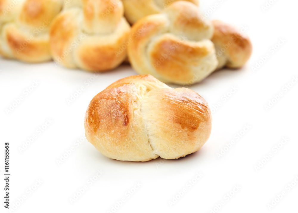 Yeast bread bun with defocused pile of buns. Golden baked yeast bread knots. Braided knot roll with egg wash. Swiss butter bread called Zopf or Challah prepared for holiday meals. Selective focus. Yeast bread bun with defocused pile of buns. Golden baked yeast bread knots. Braided knot roll with egg wash. Swiss butter bread called Zopf or Challah prepared for holiday meals. Selective focus.