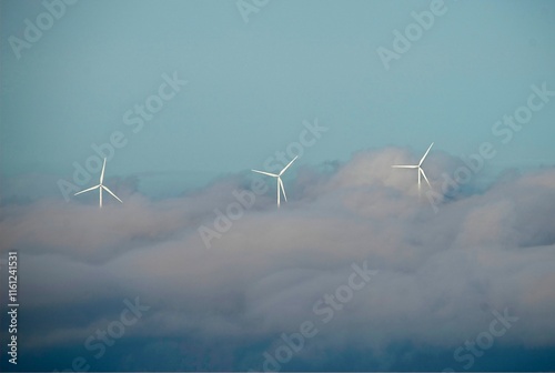three wind turbines with clouds below and blue sky on top