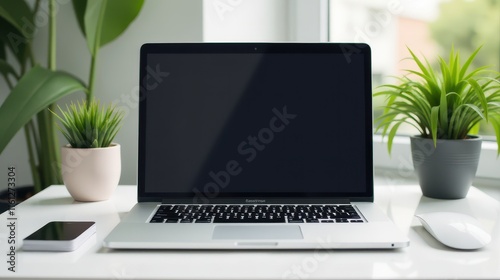 A laptop with a blank screen sits on a white desk surrounded by green potted plants and notebooks, creating a serene workspace by the window