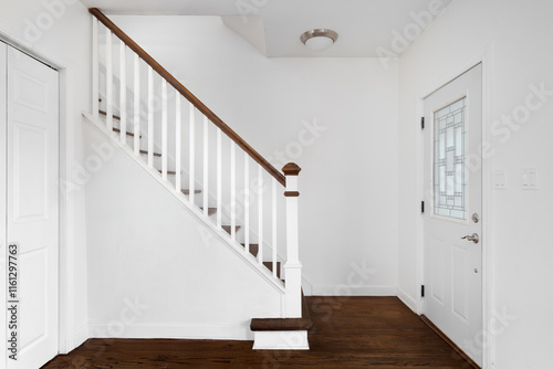 A home entryway detail with a white staircase with a wood railing and steps, white front door with a frosted glass window, and dark hardwood flooring. photo