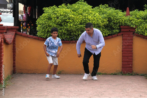 Latino dad and dark-skinned 9-year-old son play a speed race in the street, they have fun and are happy in poverty