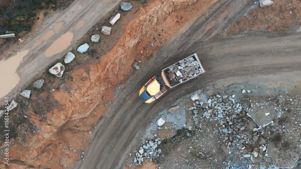 An excavator loads rock onto a massive truck, transporting it to the crusher. A quarry scene with heavy machinery running at full capacity.