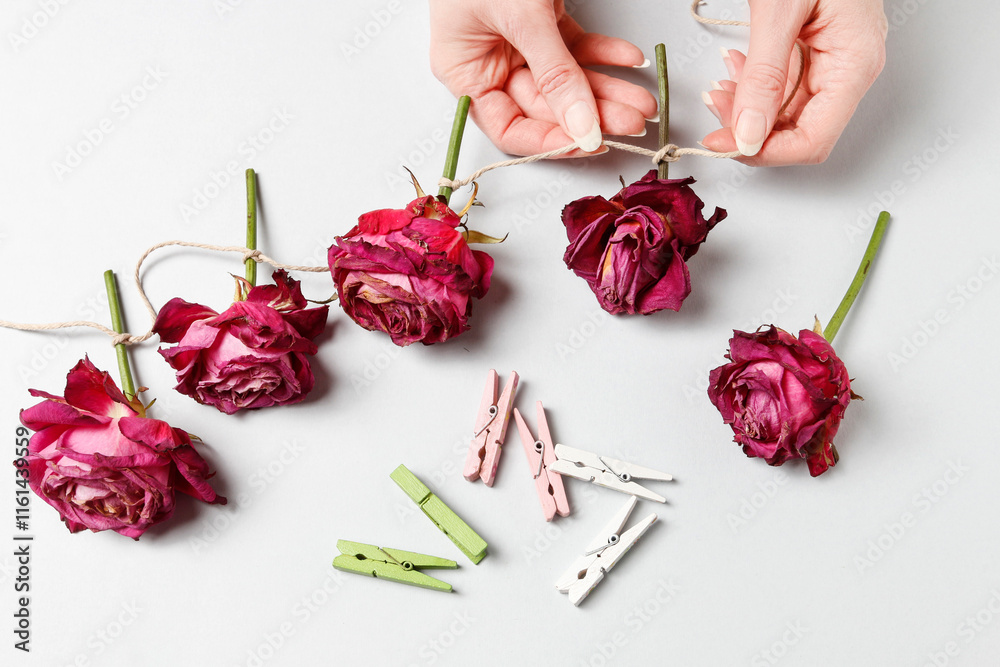 Florist at work: woman shows how to make a simple Valentine's Day decoration with semi-dry roses, string and clothes pegs. Step by step, tutorial.