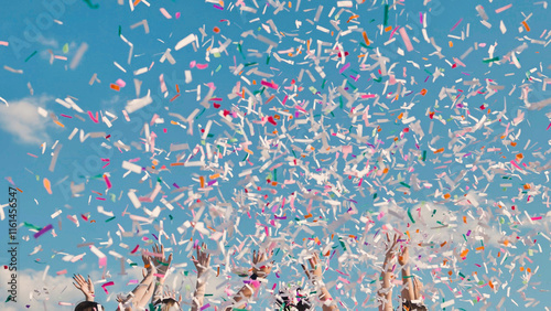 High school graduates joyfully tossing vibrant confetti in the air against a sunny blue sky