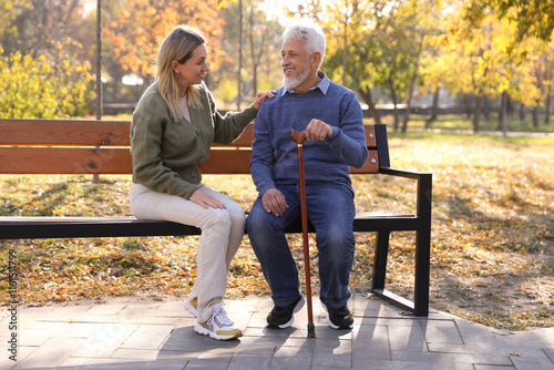 Caregiver assisting senior man on wooden bench in park. Home health care service