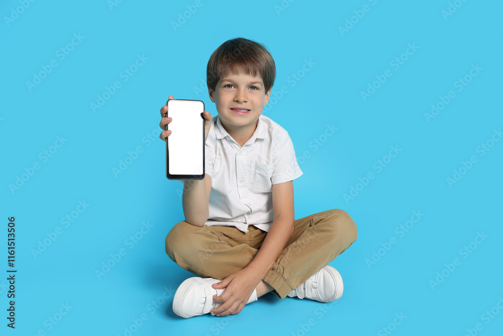 Cute little boy with smartphone on light blue background