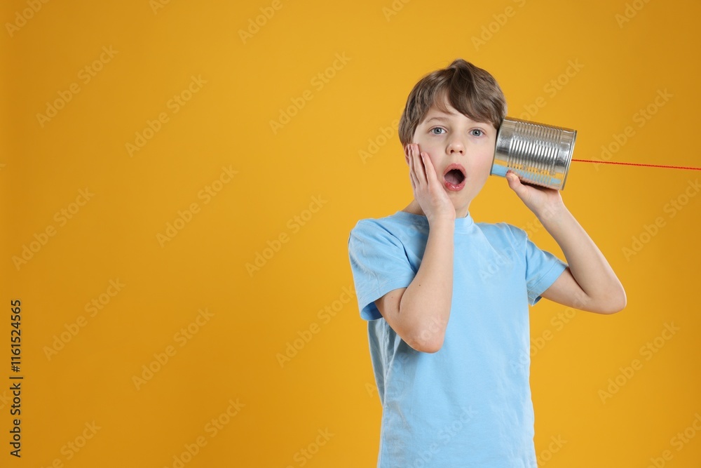 Surprised boy using tin can telephone on orange background. Space for text Surprised boy using tin can telephone on orange background. Space for text
