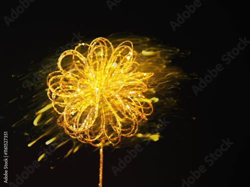 Home decoration made from golden wire and resembles abstract flower on a stem. Some reflective dots are on the metal. Black background with yellow color abstract background. Home art. photo