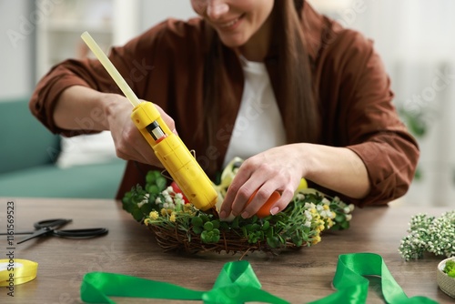 Woman with hot glue gun making craft at table indoors, closeup photo