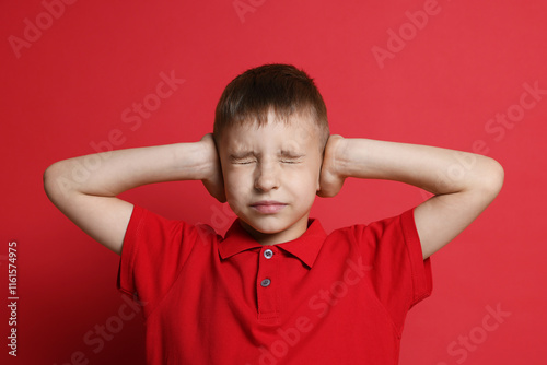 Little boy covering his ears on red background photo